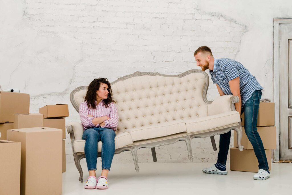 Moving Champs Team Helping a Couple Move a Sofa Into Their New Home With Packed Boxes Around.